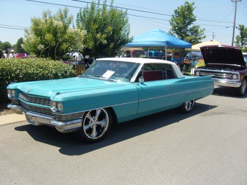 2007 Ford Mustang - A turquoise 1965 Cadillac Coupe de Ville with a white roof and chrome wheels is parked next to another vehicle.