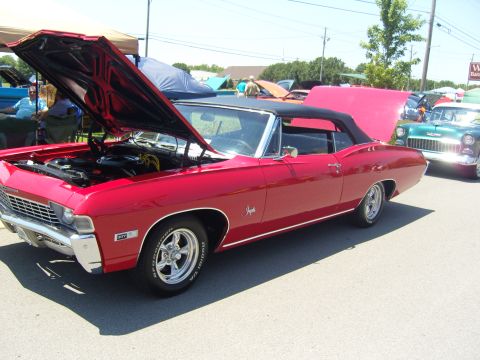 2007 Ford Mustang - A red 1967 Chevrolet Impala convertible is displayed with its hood open at a car show.
