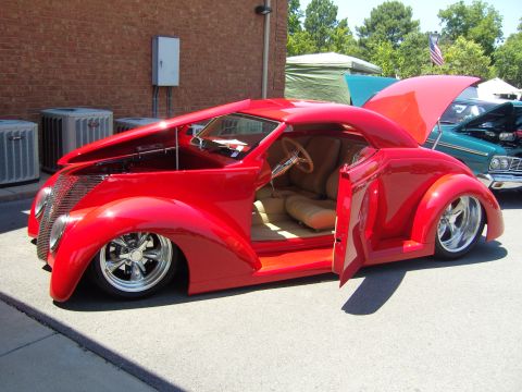 2007 Ford Mustang - A custom red hot rod coupe is displayed with its hood and driver's door open, revealing a tan interior and chrome wheels.