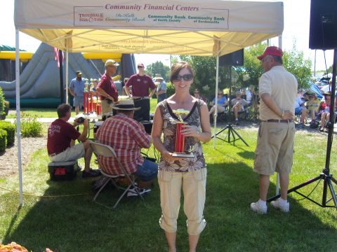 2007 Ford Mustang - A woman proudly holds a trophy at an outdoor community event, with a tent and inflatable structure in the background.