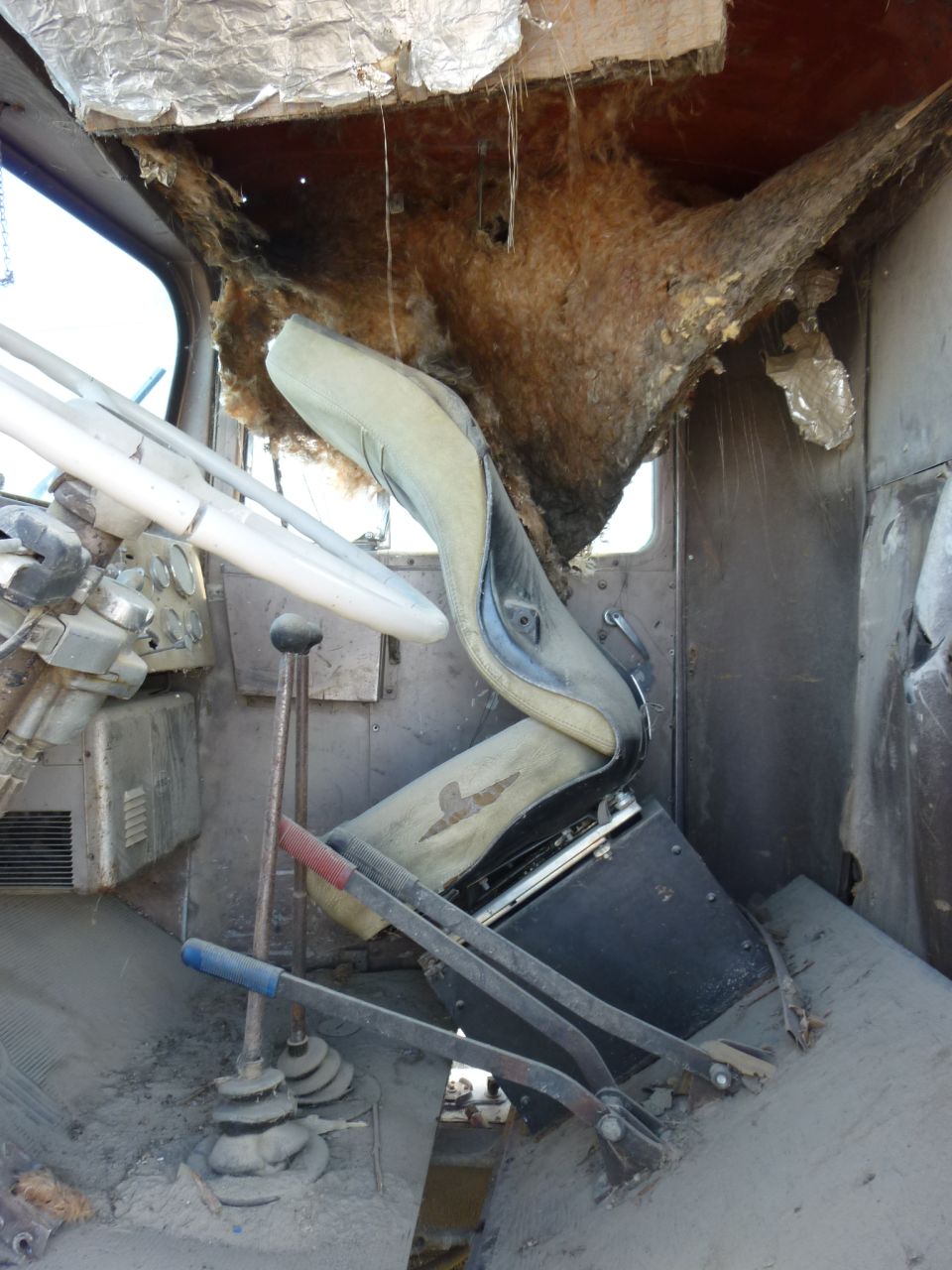 Damaged truck interior with torn insulation, worn seat, and multiple levers