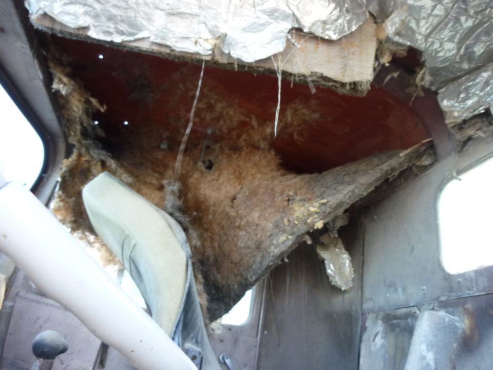 Interior of a truck cab showing damaged headliner and insulation. Seat and steering column visible