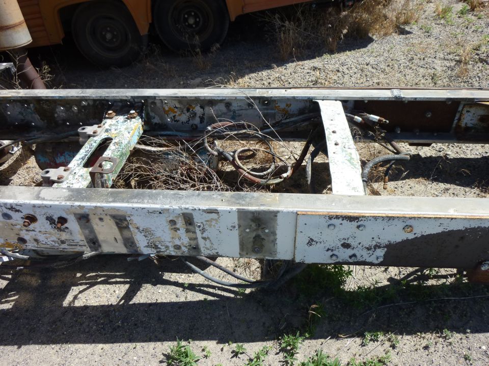 Truck frame rails with wiring and air lines visible; orange vehicle in background