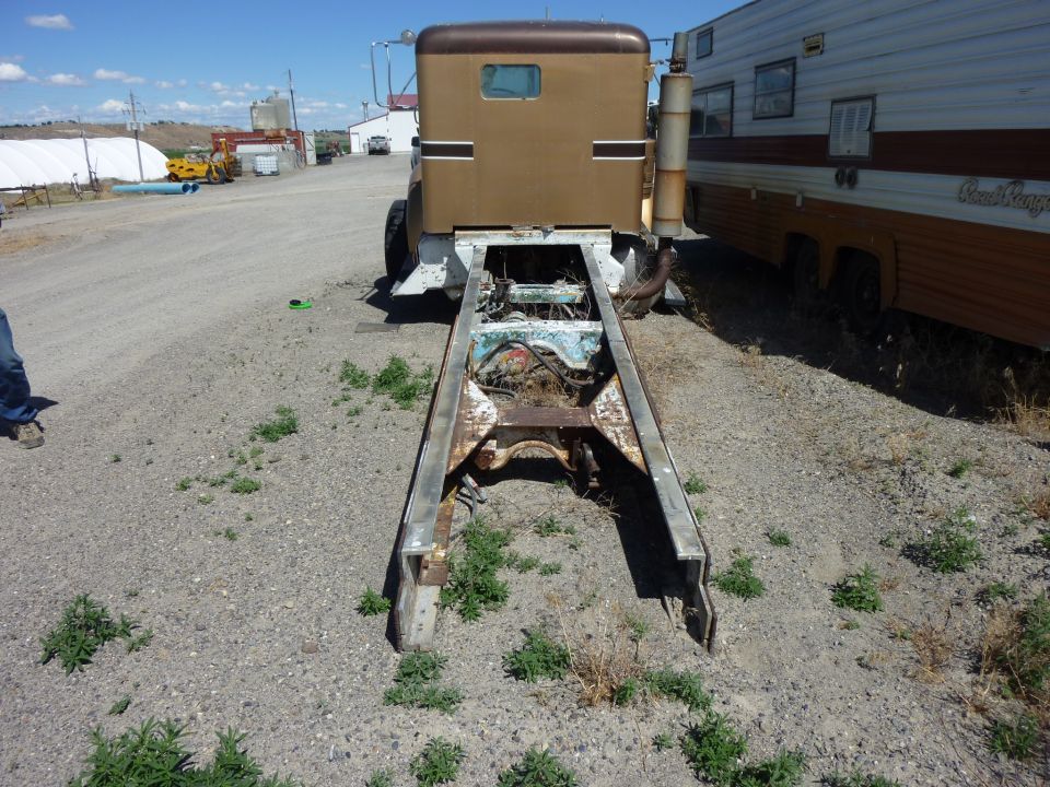 Brown truck cab and chassis, rear view. A trailer is parked to the right