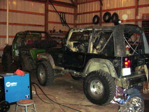1992 Ford Bronco - Two custom Jeeps are being worked on inside a garage, with a welding torch visible.