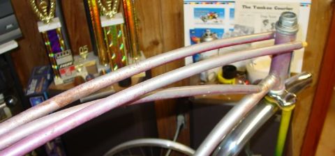 1953 Ford Mainline - A bicycle frame with multiple tubes and some visible rust is shown in a room with trophies and a newspaper.