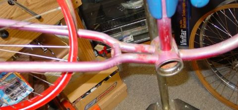 1953 Ford Mainline - Close-up of a pink bicycle frame, possibly undergoing restoration or repair, with visible spokes and some signs of wear.