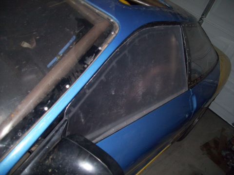 1995 Ford Probe - Close-up view of a blue car's side window, revealing a roll cage and custom metal trim.
