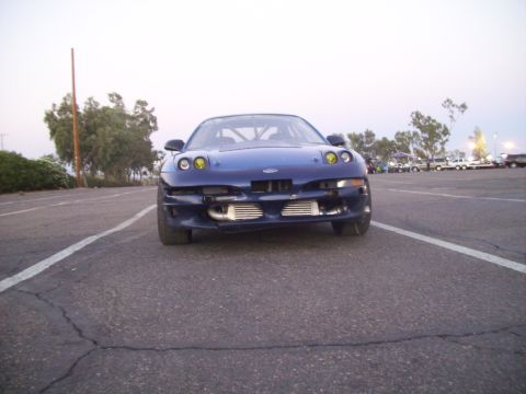 1995 Ford Probe - This modified 1995 Ford Probe is parked on asphalt with trees and other vehicles in the background.