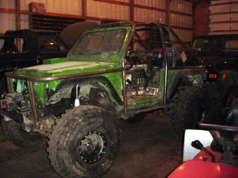 1992 Ford Bronco - A heavily modified green off-road vehicle with a roll cage and large tires sits in a garage.