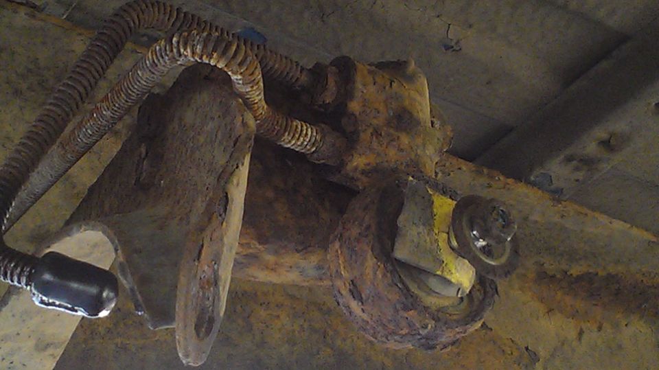 Heavily rusted suspension part with yellow markings and corrugated wiring