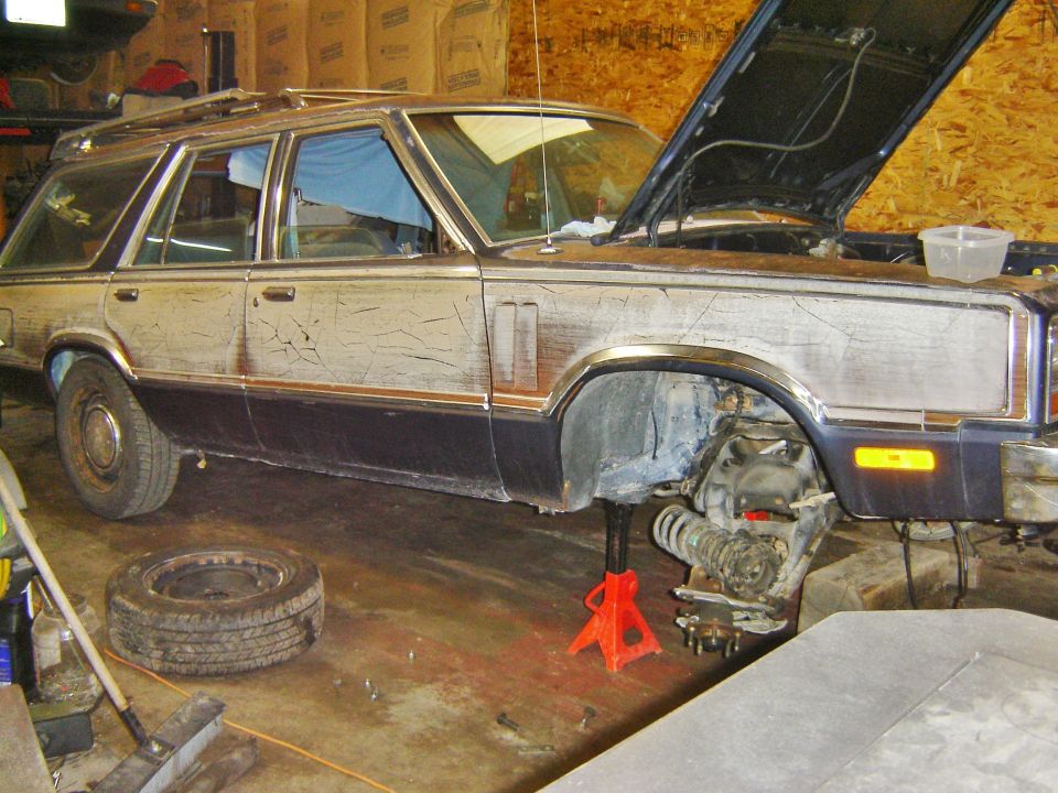 Station wagon with hood up and front wheel removed, on jack stands in a garage