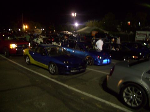 1995 Ford Probe - A two-tone sports car is parked at an outdoor event at night with many other vehicles and people present.