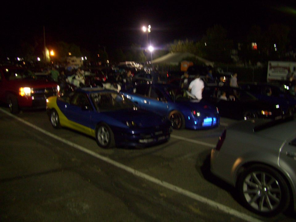 Blue and yellow sports car parked at night, other cars and people around