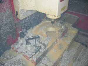 1993 Ford Taurus - A CNC milling machine is actively cutting a metal part, creating a significant amount of metal shavings and coolant spray.