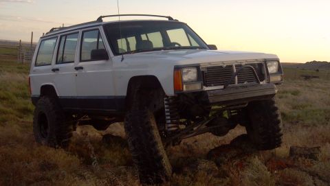 1995 Jeep Cherokee - This lifted 1995 Jeep Cherokee features oversized tires and a modified front end, captured in a three-quarter front view during golden hour.