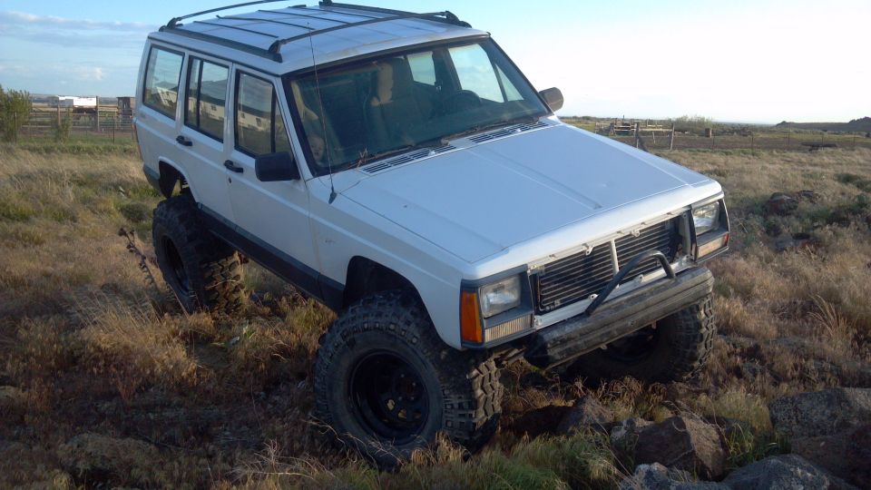 White Jeep Cherokee with large tires driving on rocky terrain