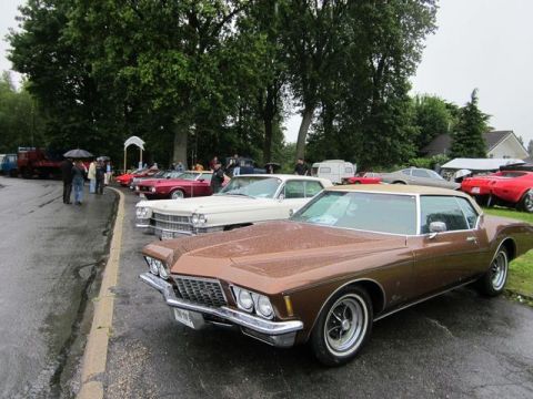 1991 Ford LTD Crown Victoria - A line of classic cars, including a brown 1973 Riviera, are parked outdoors on a wet day.