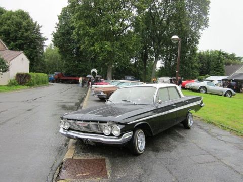 1991 Ford LTD Crown Victoria - A classic black and white Chevrolet Impala is parked alongside other vintage vehicles on a rainy day.