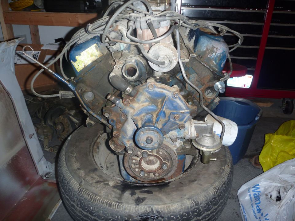 V8 engine block with distributor, water pump, and oil filter, resting on a tire