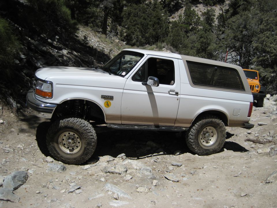 White 1996 Ford Bronco on rocky terrain, lifted suspension, tan soft top