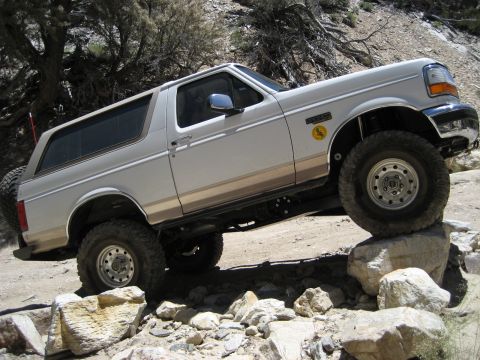 1996 Ford Bronco - A white 1996 Ford Bronco navigates a rocky, off-road trail with its tires on large boulders.