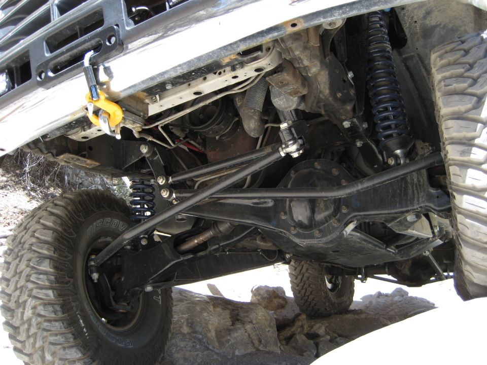 Underside view of an off-road vehicle showing suspension, differential, and large tires on rocks