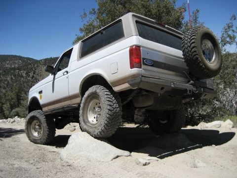 1996 Ford Bronco - A white 1996 Ford Bronco navigates a rocky off-road trail with a spare tire mounted on the rear.