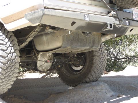 1996 Ford Bronco - The rear axle and undercarriage of an off-road vehicle are visible, with large tires mounted on rocky terrain.