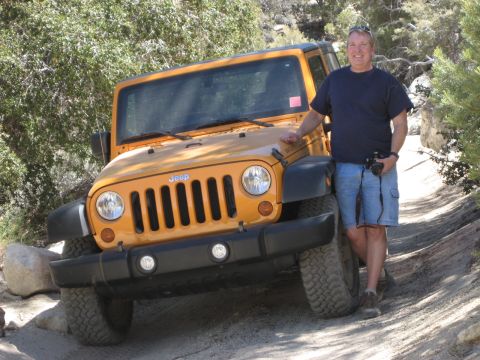 1996 Ford Bronco - A man poses with his yellow Jeep Wrangler on a dirt trail surrounded by trees.