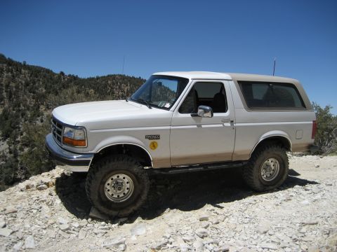 1996 Ford Bronco - A white Ford Bronco is parked on a rocky surface with a mountainous landscape in the background.