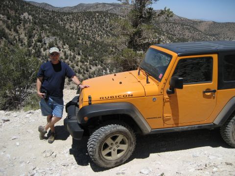 1996 Ford Bronco - A man poses with his orange Jeep Wrangler Rubicon in a scenic, mountainous landscape.