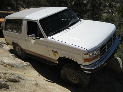 1996 Ford Bronco - A white 1996 Ford Bronco navigates a rocky off-road trail, with another vehicle visible in the background.