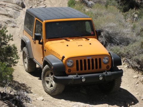 1996 Ford Bronco - This Jeep Wrangler Rubicon is driving on a rocky, off-road path with sparse vegetation.