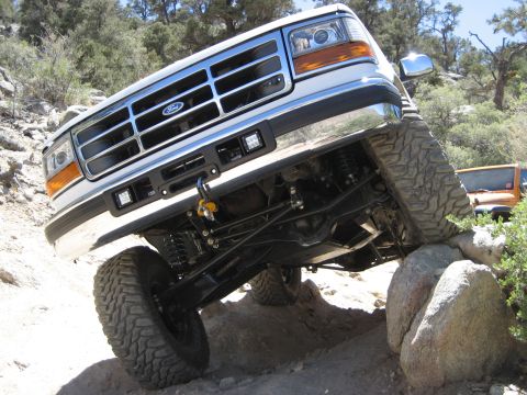 1996 Ford Bronco - White Ford F-Series truck navigates rocky terrain with its front end angled upwards.