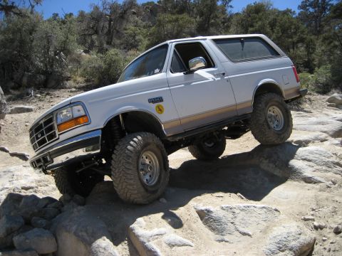 1996 Ford Bronco - A white 1996 Ford Bronco navigates a rocky trail with its suspension flexed.