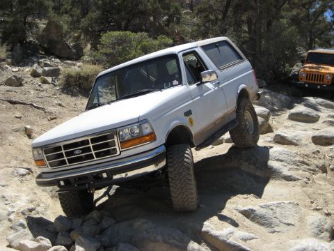 1996 Ford Bronco - A white 1996 Ford Bronco navigates a rocky trail, with an orange Jeep visible in the background.