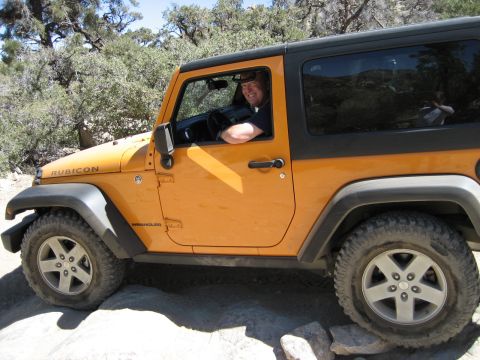1996 Ford Bronco - Driver smiles from inside an orange Jeep Wrangler Rubicon on a rocky off-road path.