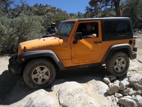 1996 Ford Bronco - A Jeep Wrangler Rubicon navigates a rocky trail under a clear blue sky.