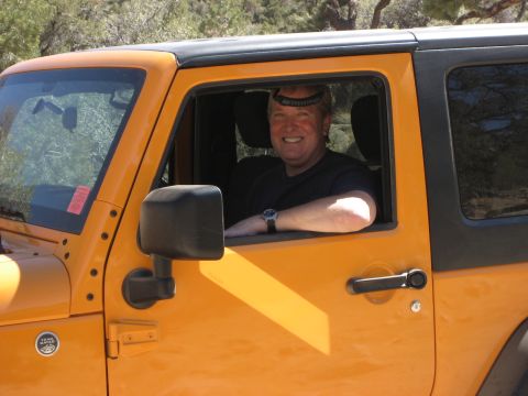 1996 Ford Bronco - Man smiles from the driver's seat of an orange Jeep Wrangler.