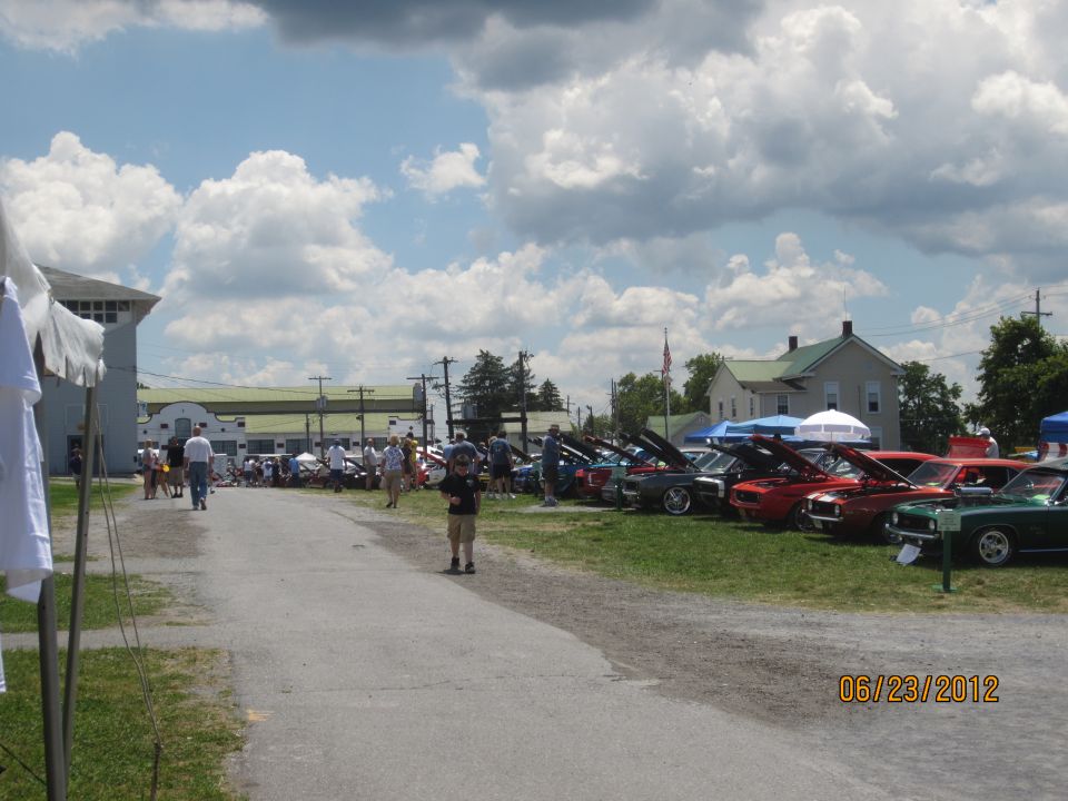 Cars lined up on grass at an outdoor event, with people walking around. Date stamp reads 06/23/2012