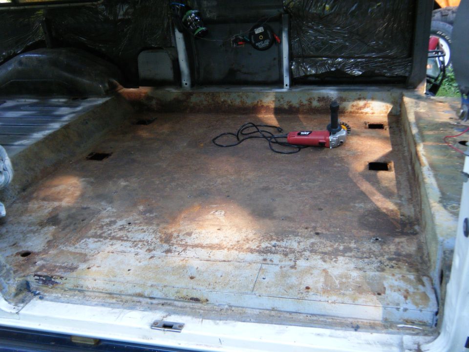 Interior cargo area of a van with rusted floor, insulation on walls, and a red angle grinder