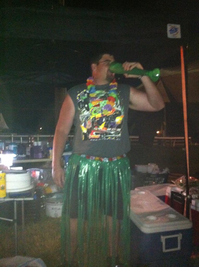 Man in Hawaiian shirt and grass skirt drinking from a green cup