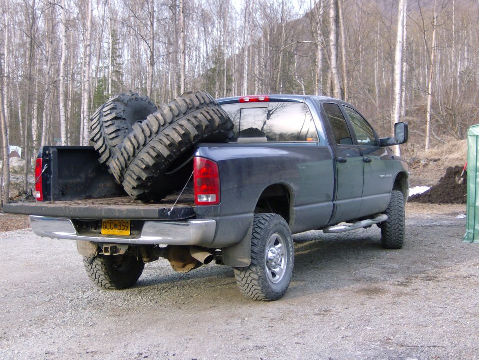 Pickup truck bed loaded with two large off-road tires. Side view