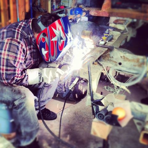 1983 Chevrolet C/K Pickup - A person welds on a vehicle frame in a cluttered garage setting.