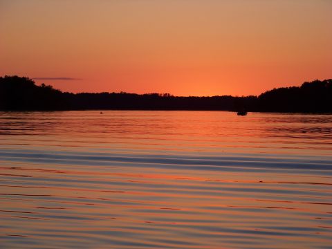 1996 Ford F-150 - A sunset paints the sky with orange and pink hues over a calm lake, with two boats visible in the distance.