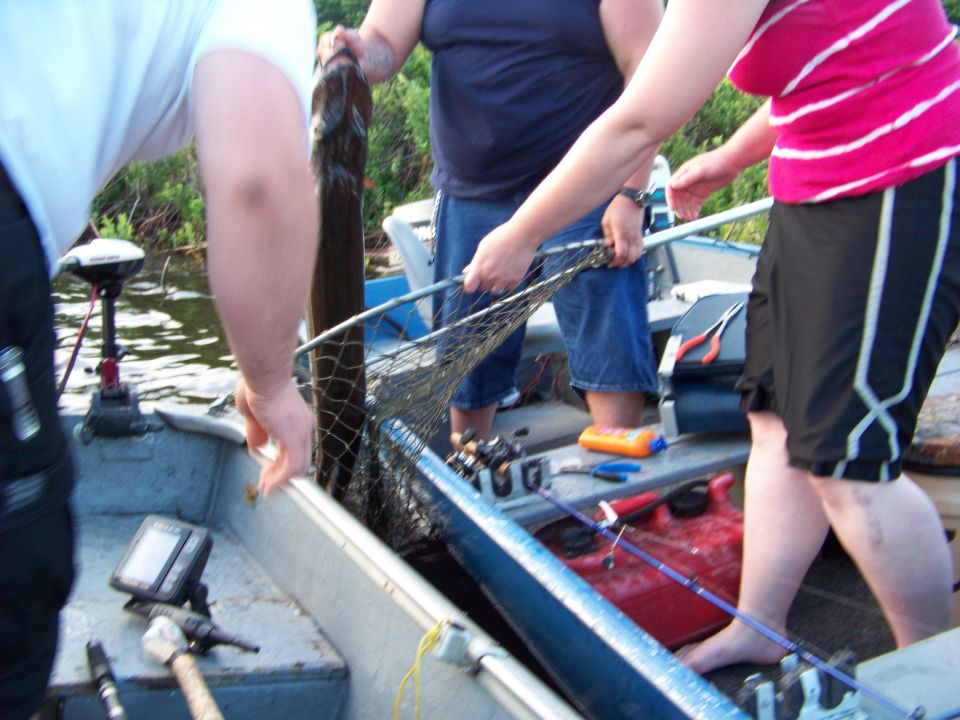People in a boat holding a large fish and a net