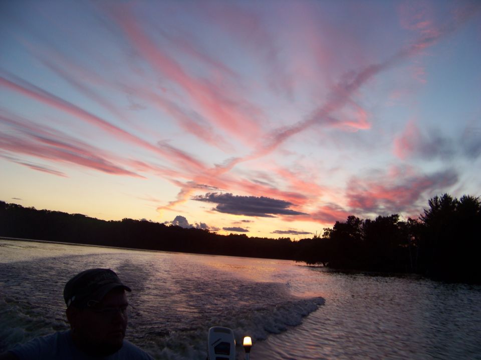 Person in hat on boat at sunset with pink clouds