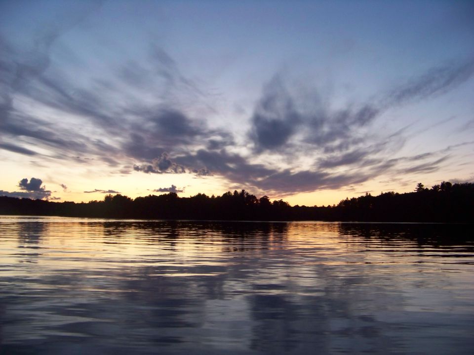 Lake with silhouetted trees and a dramatic sunset sky with clouds