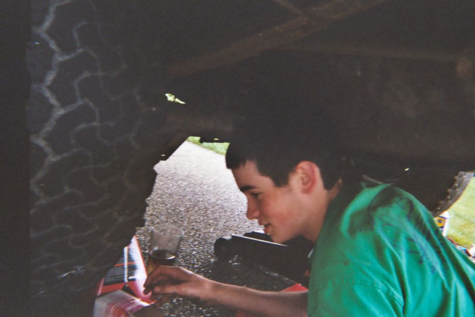 Young person in green shirt working under a vehicle on a driveway